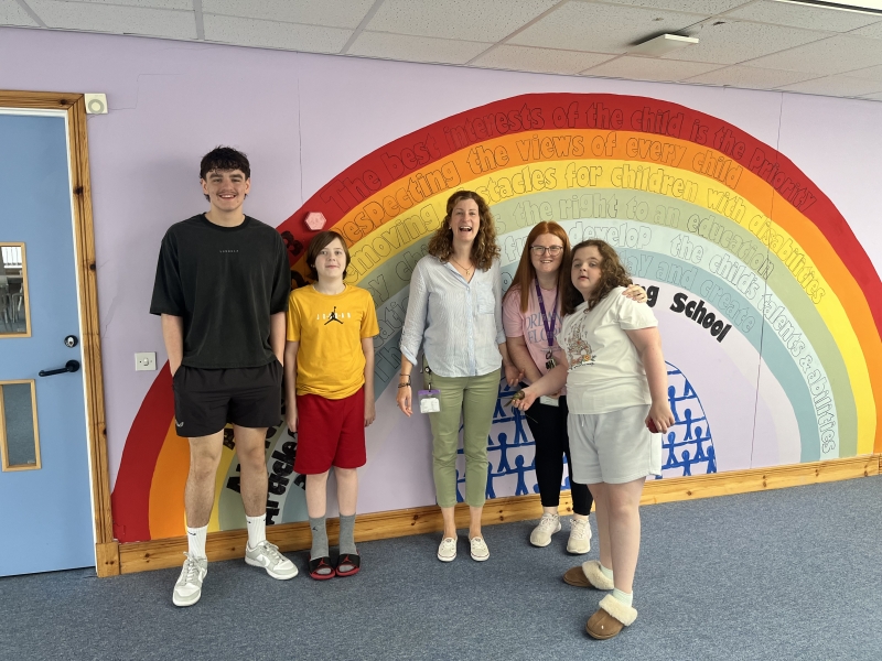 pupils Kyran McRoberts, Jay Doyle and Ava Burrows standing beside the New Struan 'Rights Respecting Schools Rainbow' alongside Headteacher, Deborah Henderson, and Classroom Assistant, Jenn Day, the school's Rights Respecting Schools Champion.