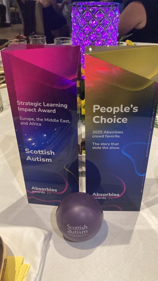 Two awards sit on a table for Scottish Autism winning in the 2025 Absorbies Award. One is for Strategic Learning Impact (EMEA) and the other for People's Choice
