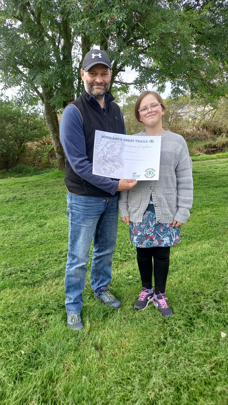 Image is of Our Spectrum Adventures' duo Eve and her dad, Ian, with Eve’s certificate for completing all of Scotland’s Great Trails. Image with credit to NatureScot